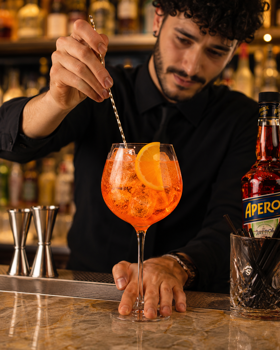 Bartender removiendo un Aperol Spritz en copa de balón junto a la botella de Aperol