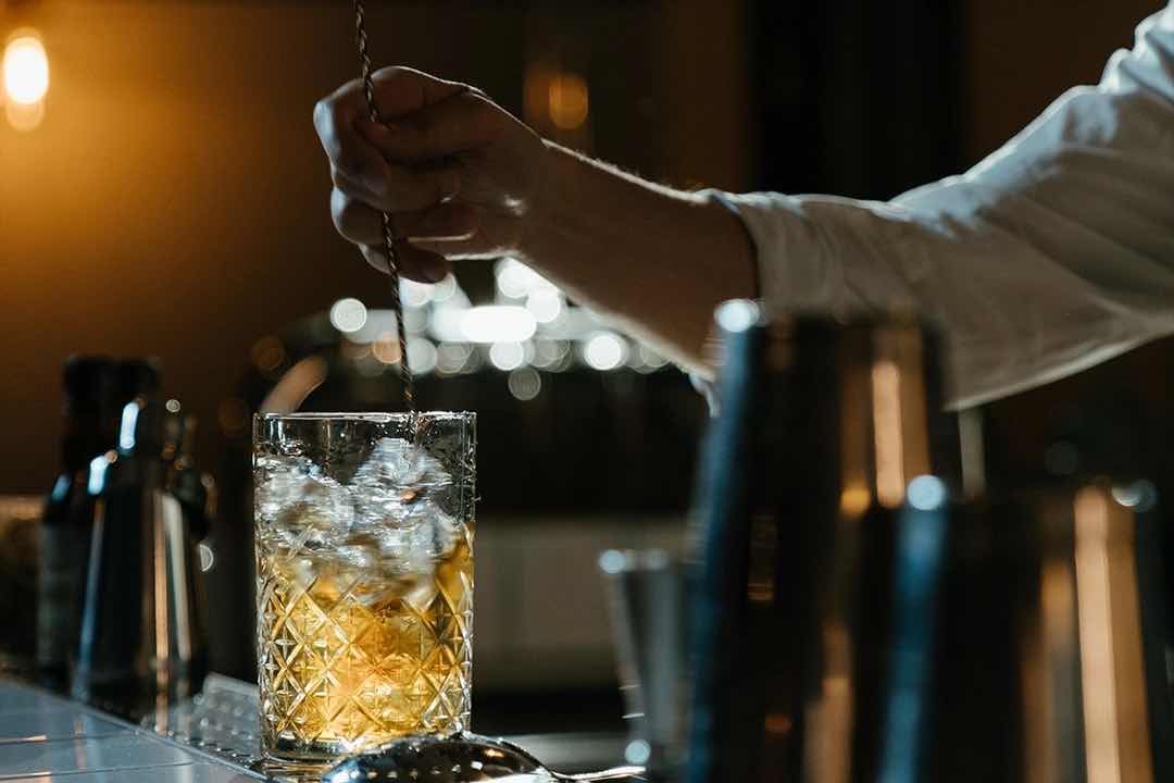 Camarero mezclando un cóctel en un vaso de cristal.