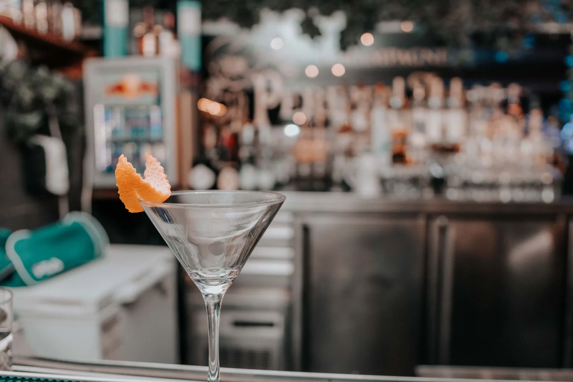 Cóctel martini con piel de naranja sobre la barra de un bar
